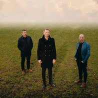 3 men standing slightly apart on grass with misty background