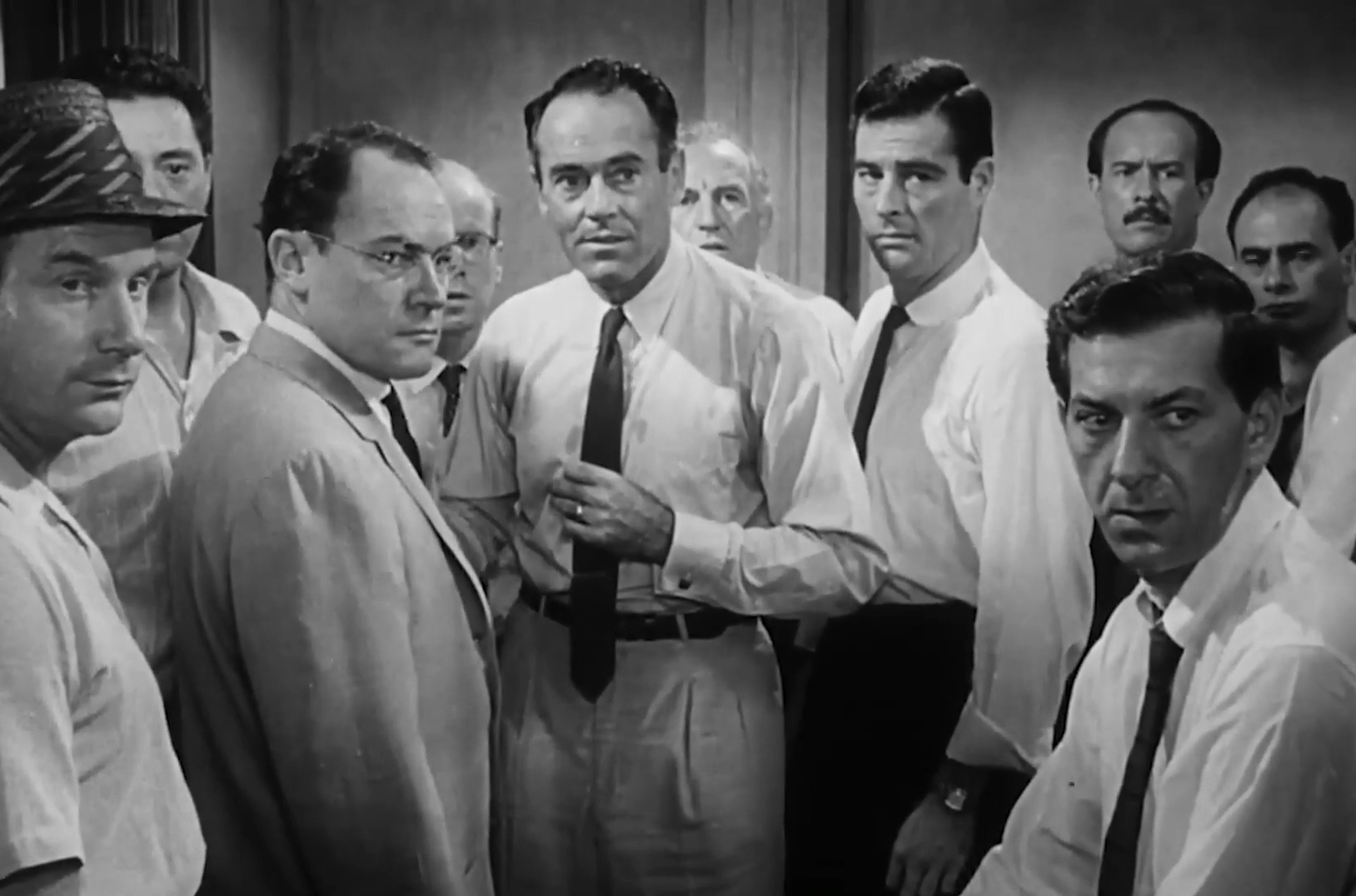 Black and white photo of group of men from the 1950s, all in white shirts with dark ties, looking serious.