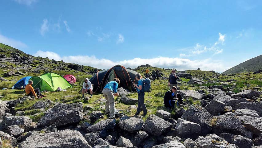 A group of climbers setting up camp up a mountain with coloured tents visible in the picture
