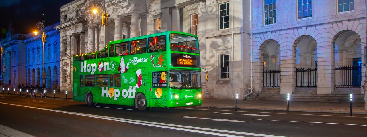 A green double decker bus at night outside old city buildings