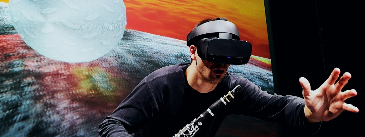 Music Current 2026 _ Ressi Benes, a man wearing a VR headset and holding a clarinet is reaching out with his other hand.