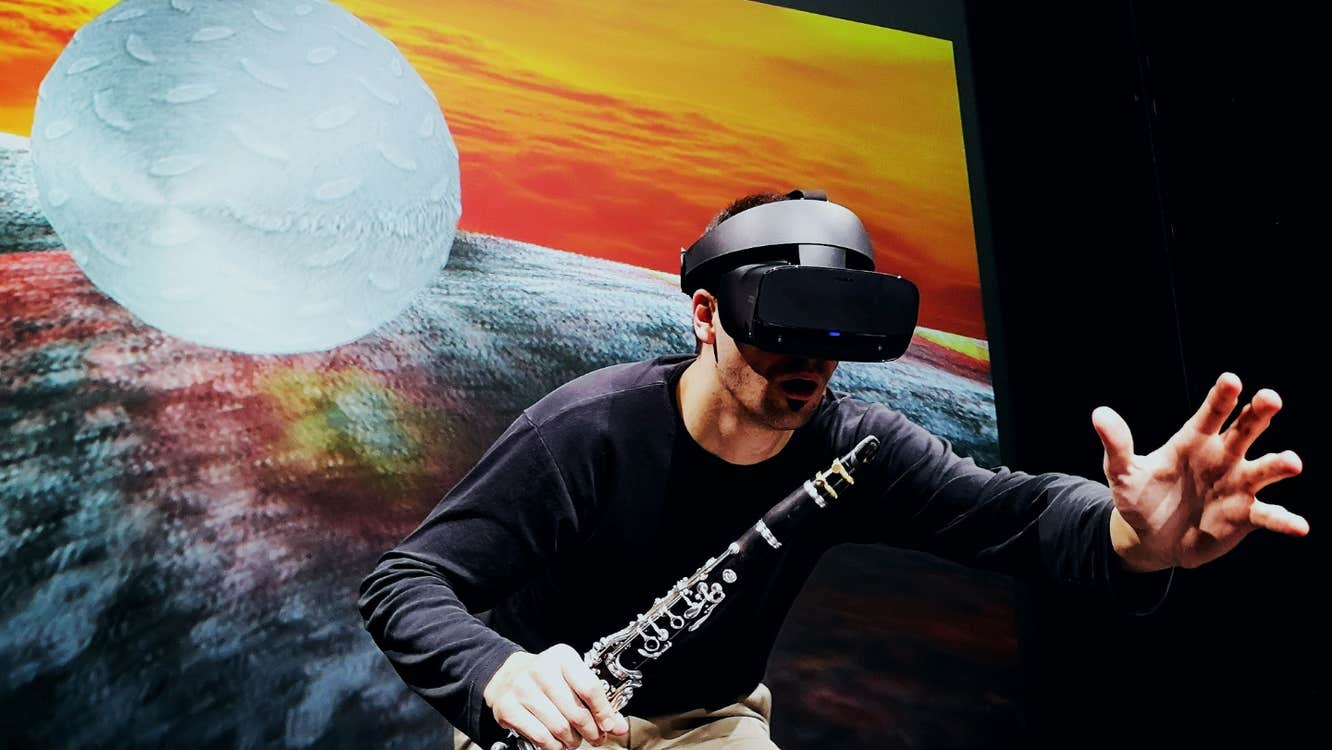 Music Current 2026 _ Ressi Benes, a man wearing a VR headset and holding a clarinet is reaching out with his other hand.