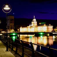 Riverside walkway at night with a building lit up in the background