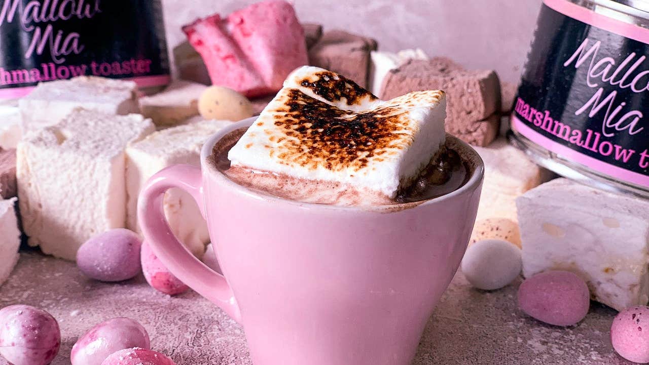 Marshmallow sitting on top of drinking chocolate in a pink mug surrounded by other pink items