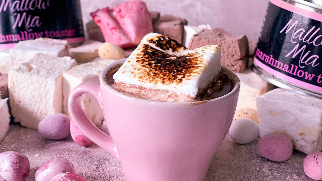 Marshmallow sitting on top of drinking chocolate in a pink mug surrounded by other pink items