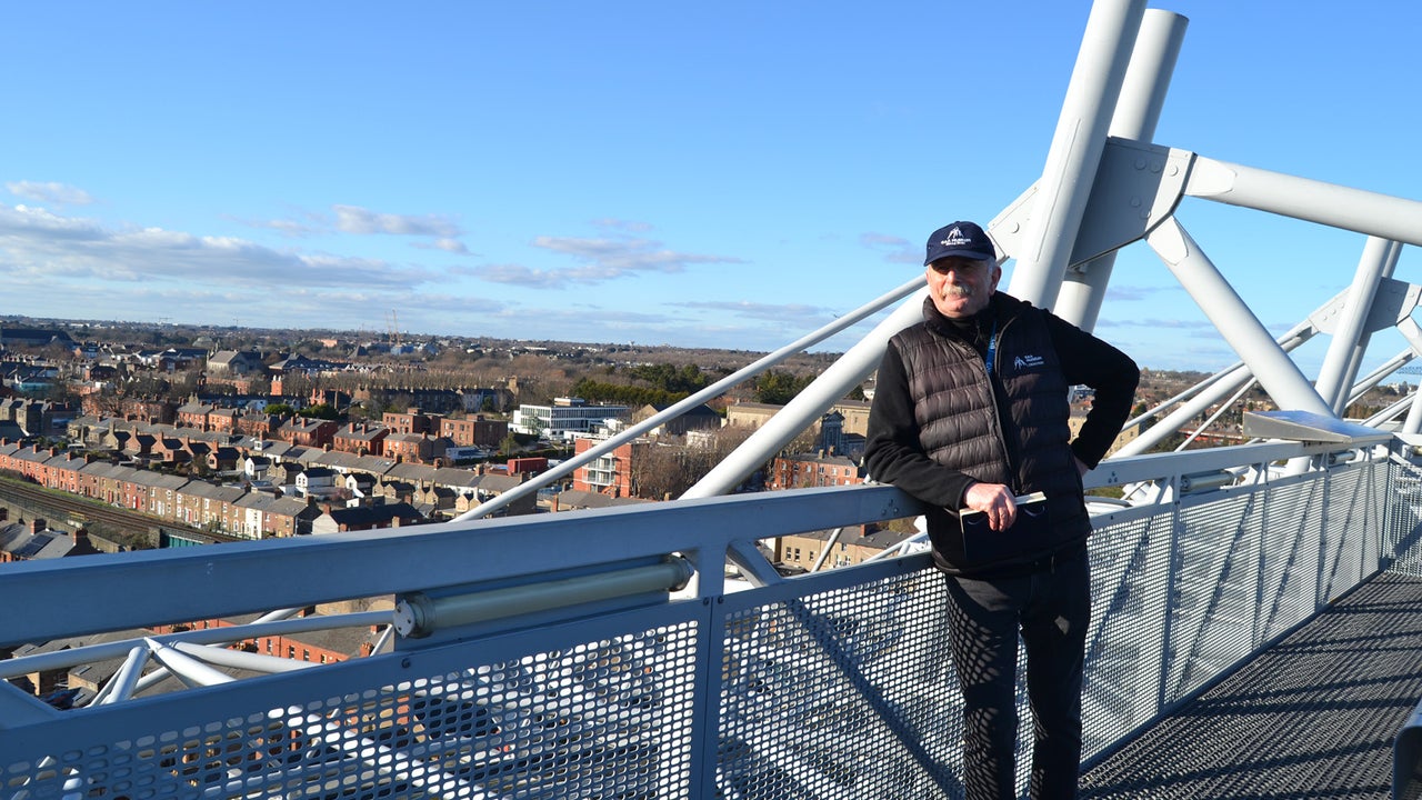 A man leaning on a rail overlooking a city on a sunny day.