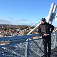 A man leaning on a rail overlooking a city on a sunny day.