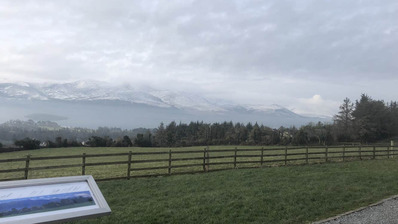 Wooden fence through a green field with snow capped mountains in the background