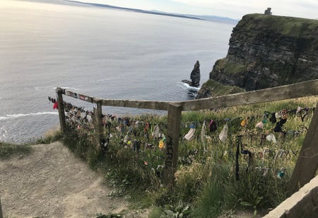 Sandy path leading to the sea with a wooden rail greenery and cliffs to the right