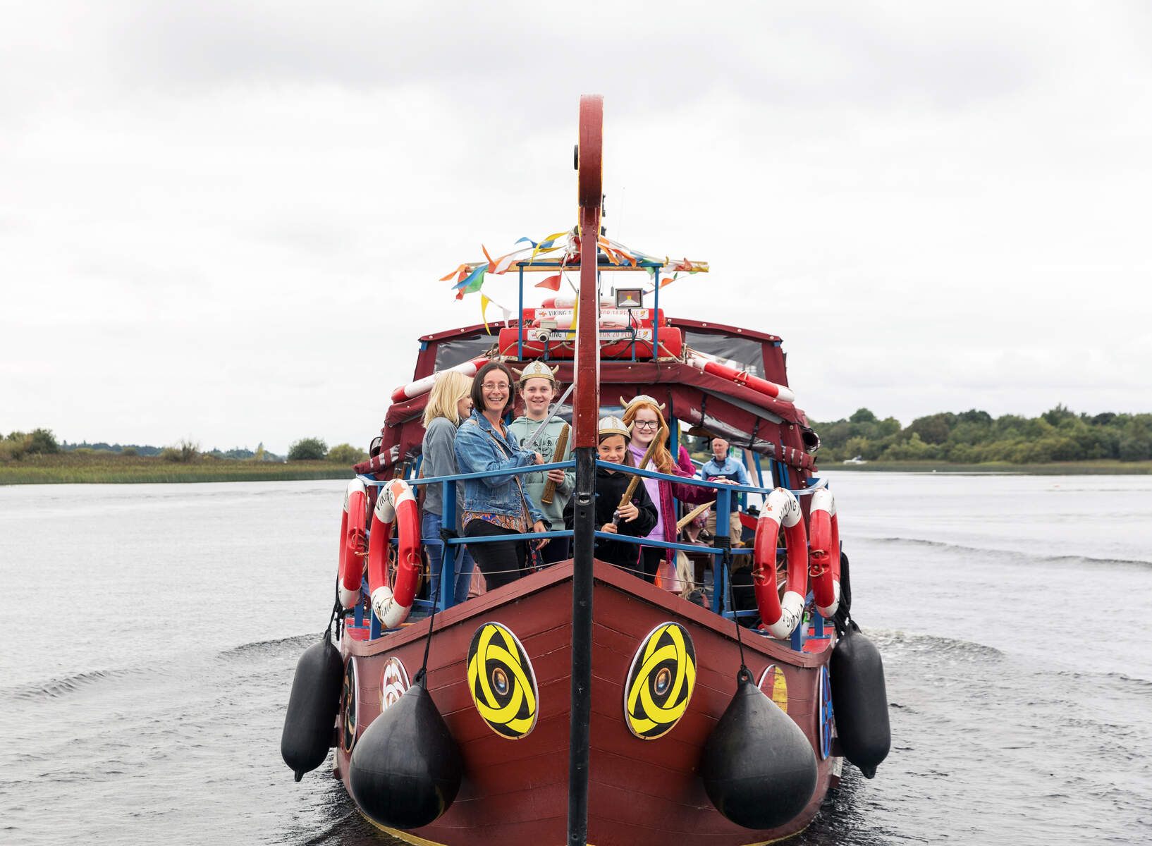 Image of Viking Ship Athlone with people standing at the bow of a small brown ship on the water.