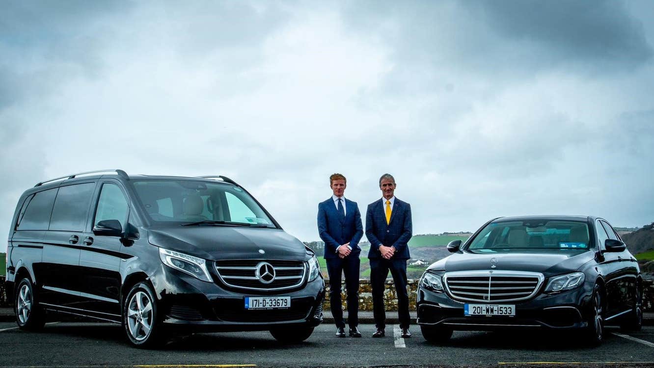 Two people in suits standing between two luxury cars
