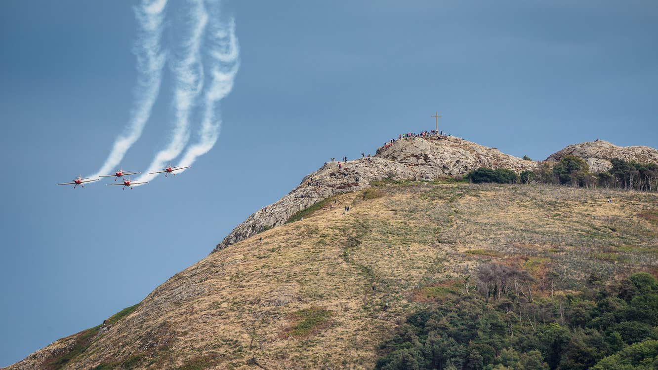 A large rocky hill with 4 jets with white plumes flying in formation to the left.