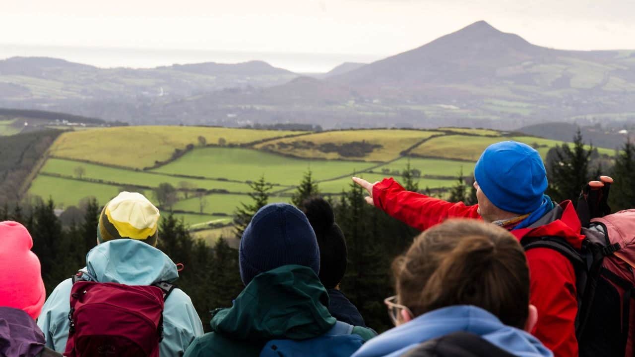 A hiking guide points out a distant feature to a group of hikers