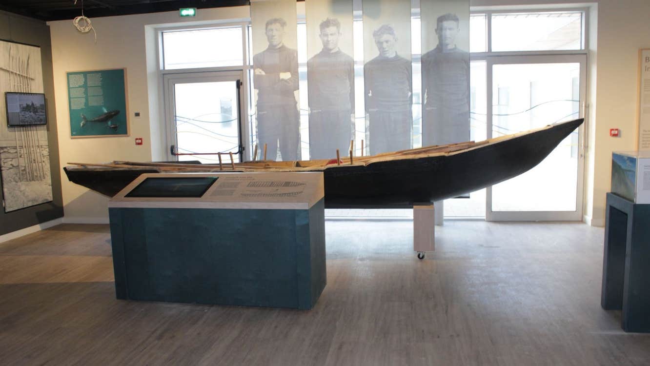 A display featuring a currach boat with images of fishermen in the background