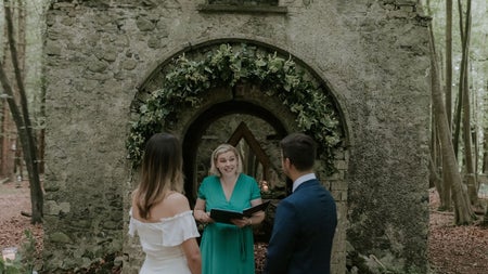 A bride and groom at a ruined archway standing in front of a celebrant
