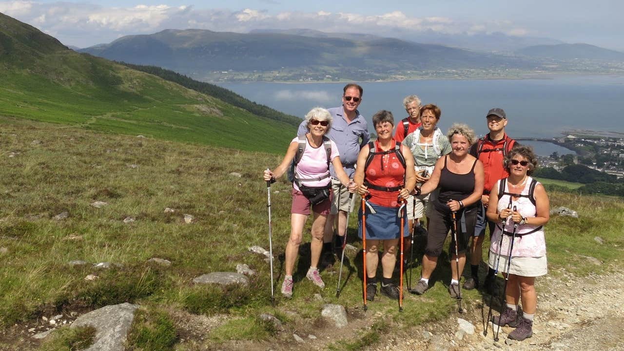 A group of walkers posed on a hill with a coastal view behind them