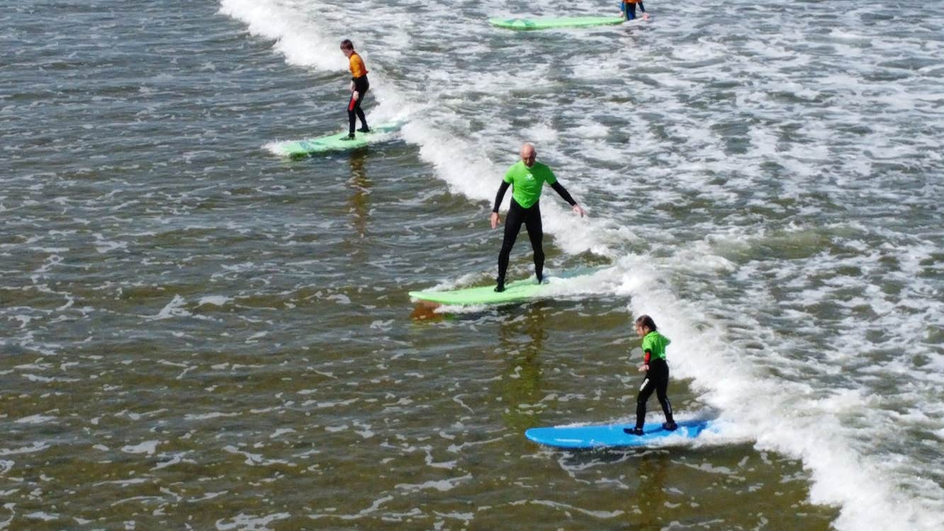 Four people wearing wetsuits surfing on blue and green surf boards