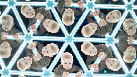 A toddler peering through a triangular tunnel lined with mirrors giving the illusion of many more toddlers