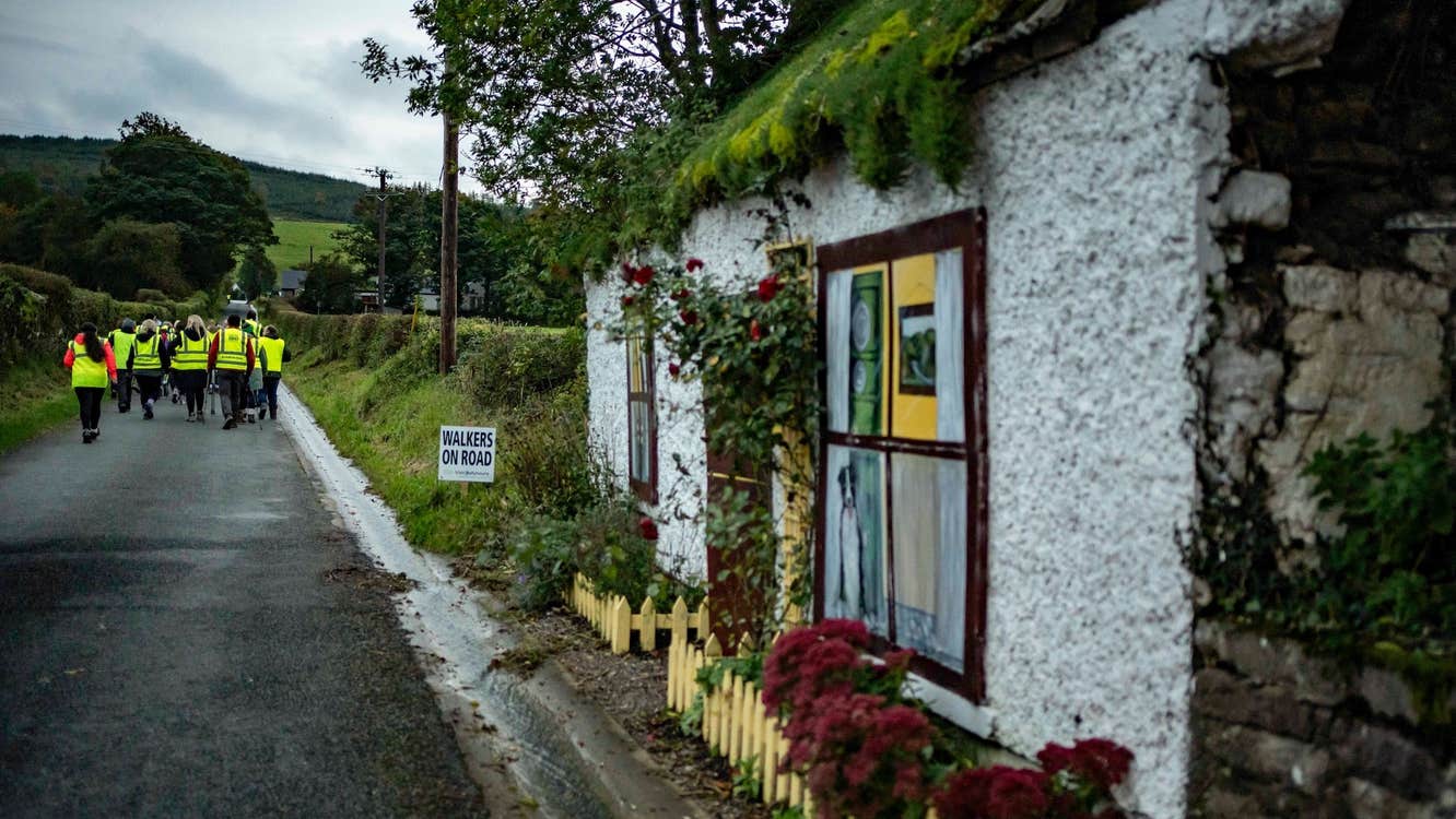 Looking down a country lane with group in hi-vis jackets walking away and old cottage in the foreground.