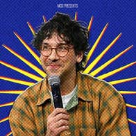 American comedian and writer, Rick Glassman - a smirking man holding a mic up to his chin.