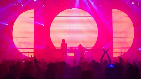 Brightly lit stage with a dj standing at his turntables