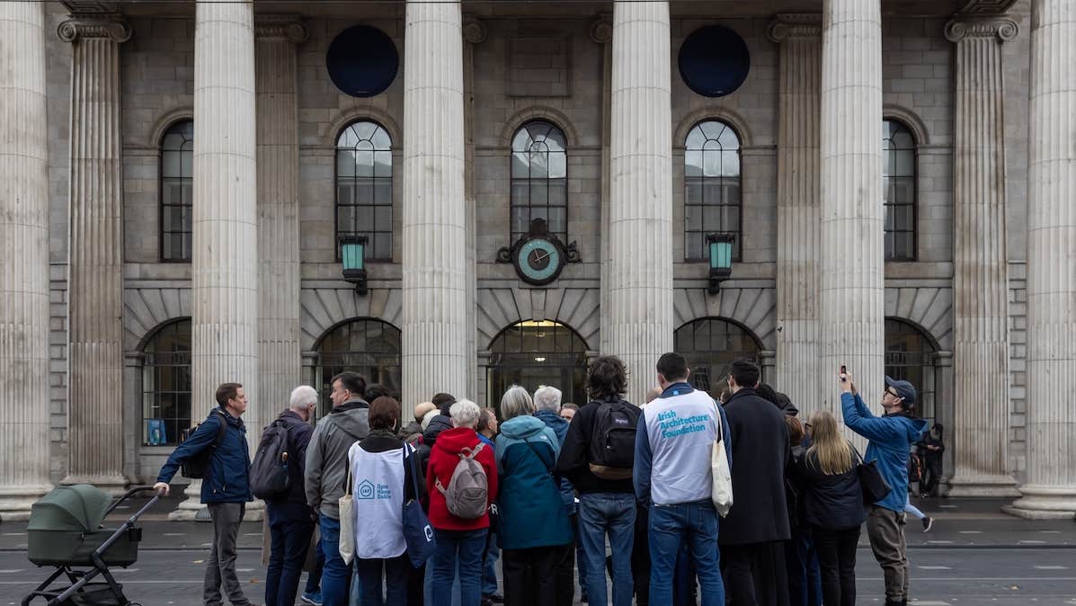 A group of people standing in front of the facade with pillars of grand building.