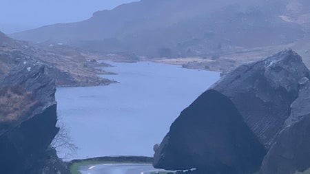 Road leading to the sea with large rocks either side and mountains in the background