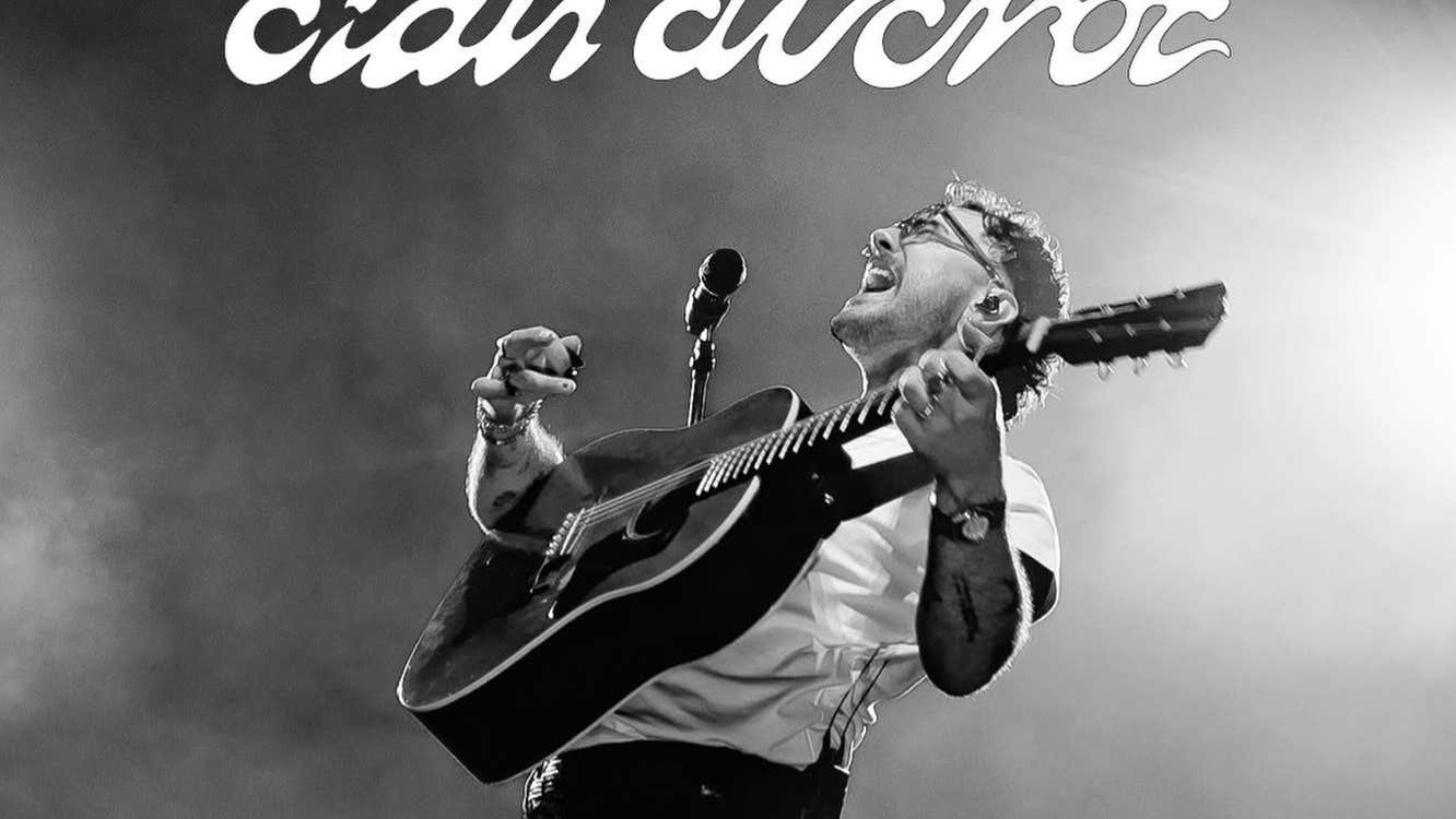 A man with a guitar performing with head thrown back, singing.
