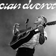 A man with a guitar performing with head thrown back, singing.