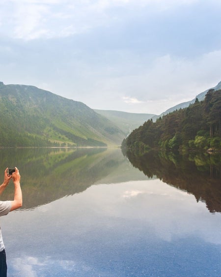 A man takes a photo across a lake and valley using a camera