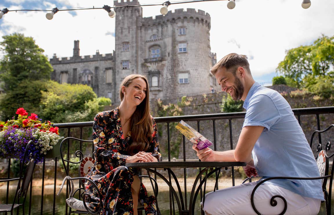 A couple sitting at a table with Kilkenny Castle in the background in County Kilkenny.