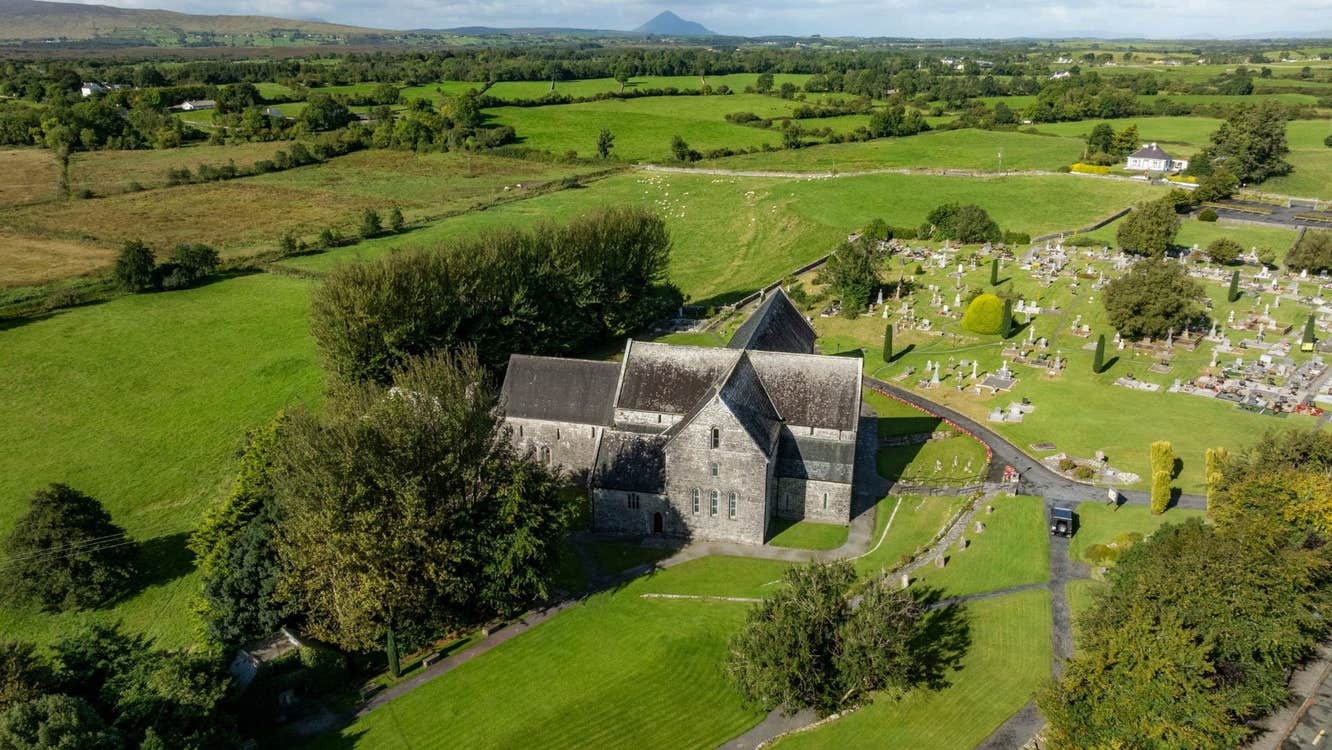 Aerial view of an abbey with a graveyard surrounded by fields