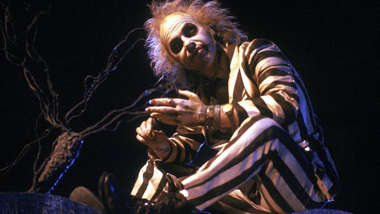 Beetlejuice is sitting by a tree, looking up at something.