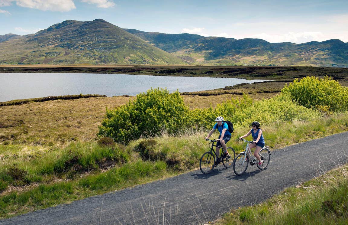 Two people cycling on The Great Western Greenway beside the sea in Mayo