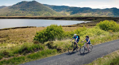 Two people cycling on The Great Western Greenway beside the sea in Mayo