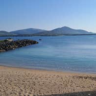 A sandy beach beside clear blue water with distant mountains under a bright sky