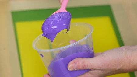 Hand holding a plastic container with purple ink and a pink spoon