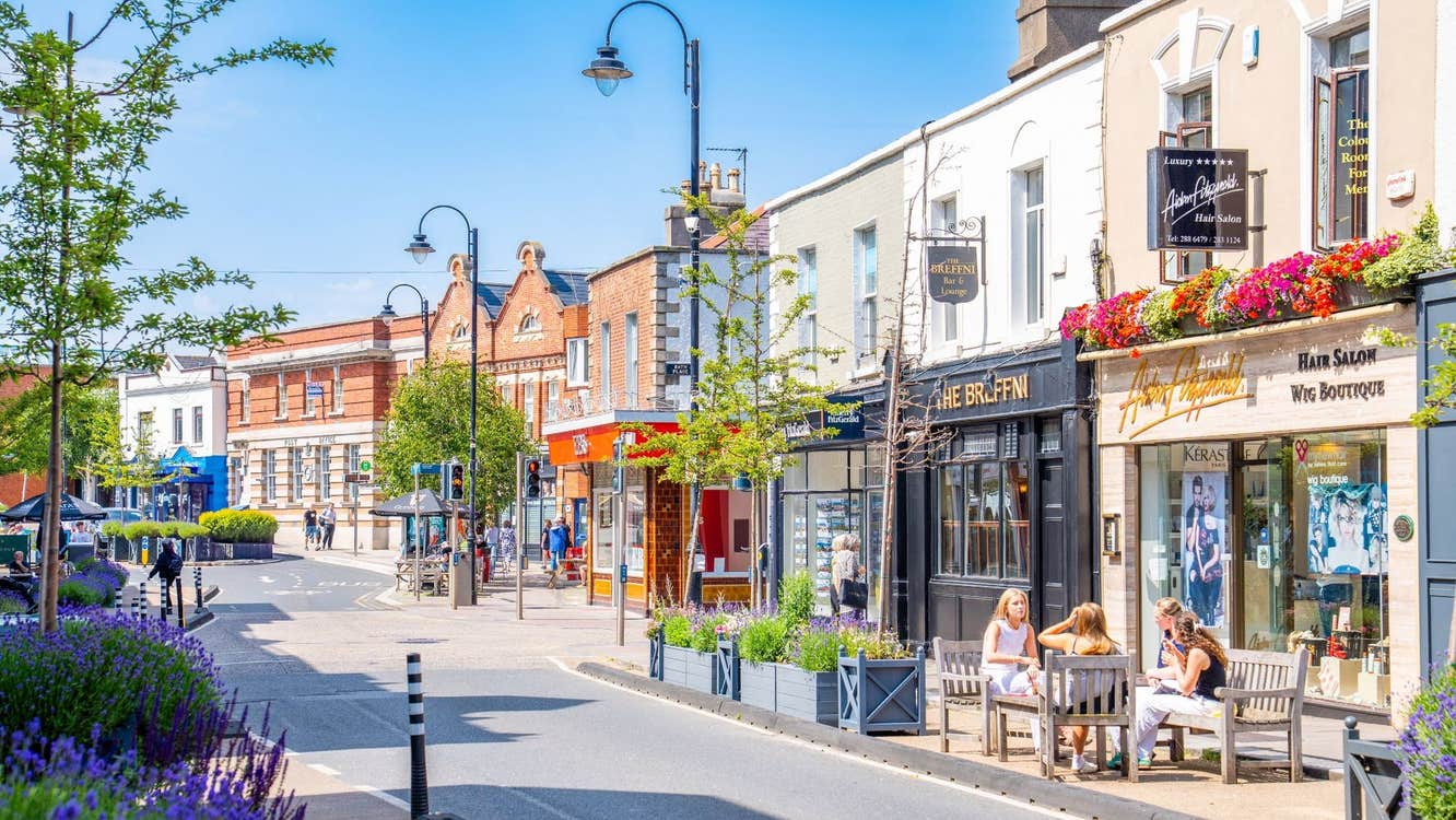 Colourful shopfronts on a Blackrock Village street with trees and planters