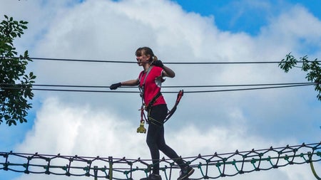 A young woman midway across a high rope walkway