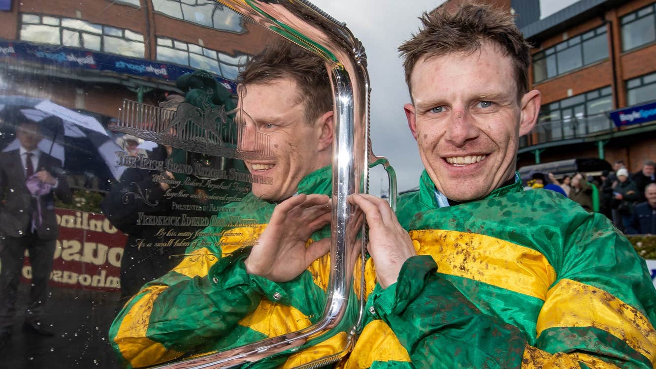 Jockey in a green and gold top holding a silver tray shaped award