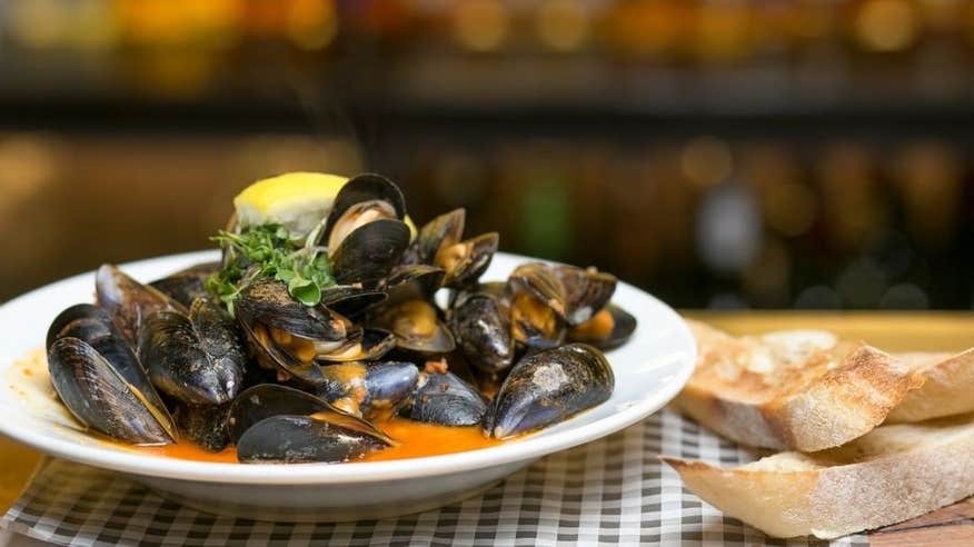 A bowl of mussels and slices of bread.