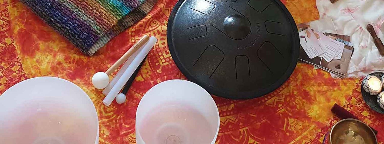 White, opaque glass bowls on a red and gold table cloth with small gongs and a stripy knitted piece of cloth.