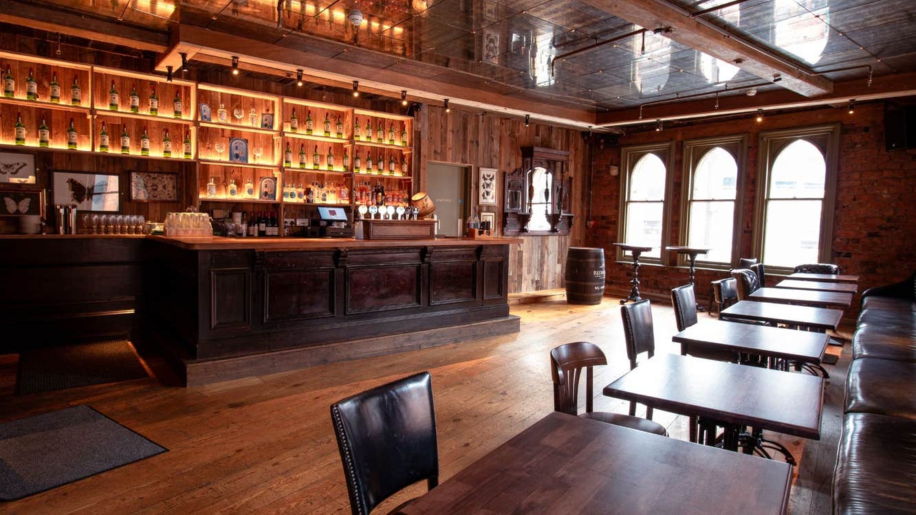 Interior of a traditional pub featuring a wooden bar with exposed brick walls and large arched windows