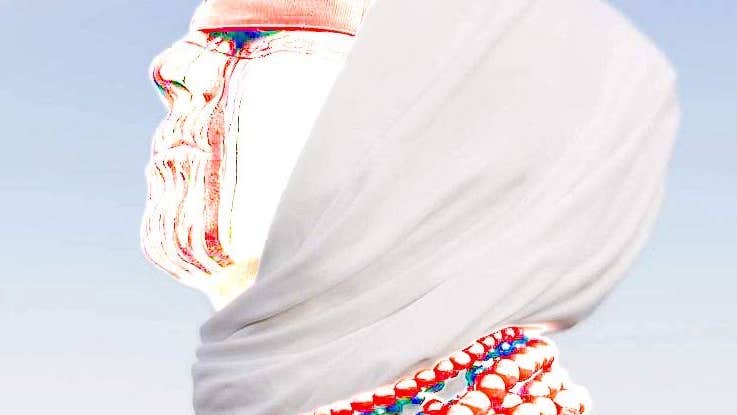 Viktoria Kondratieva wearing a headscarf, blindfold, bead necklaces and red and white make-up.