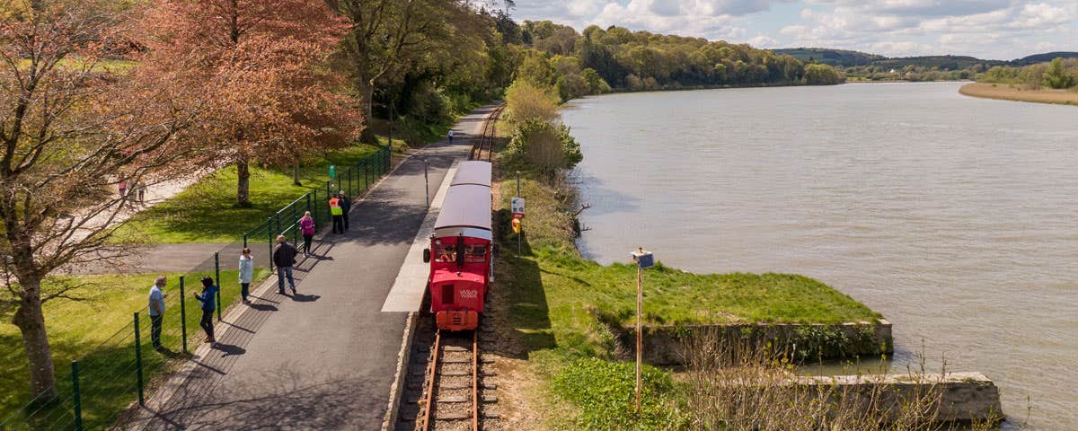 Train travelling along the Waterford Suir Valley Railway line with water beside it