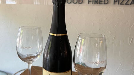 An Italian bottle of champagne with two glasses on a table with a restaurant name on the wall behind them