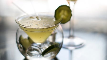 Two cocktail glasses with a clear liquid garnished with a slice of cucumber