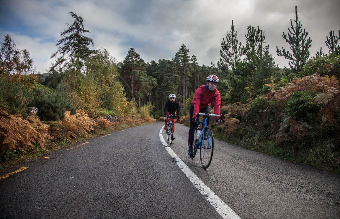 Two cyclists in a forest on a tarmac road.