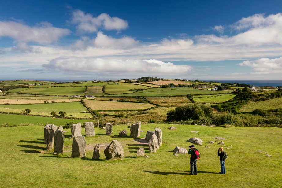 Two visitors taking pictures of Drombeg Stone Circle on a sunny day in County Cork