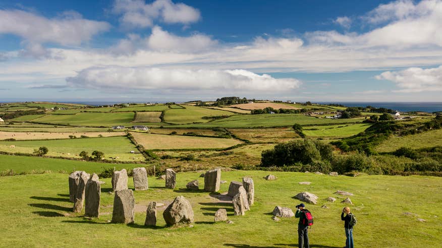 Two visitors taking pictures of Drombeg Stone Circle on a sunny day in County Cork